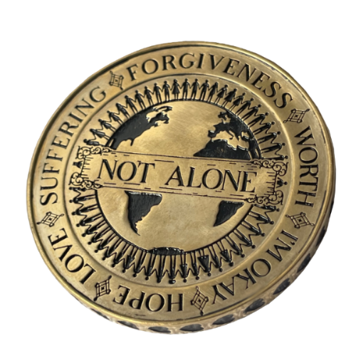 Angel Aberdeen – Human Being Coin in brass – back engraved with Not Alone, surrounded by people holding hands around the globe, additional words including Love, Suffering, Forgiveness, and I'm Okay
