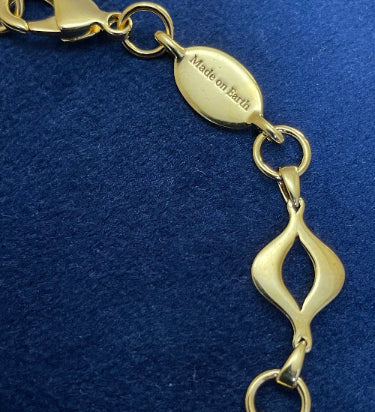 Detail of engraved “Made on Earth” tag beside lobster clasp on the gold-plated Sacred Mandorla Bracelet by Angel Aberdeen.