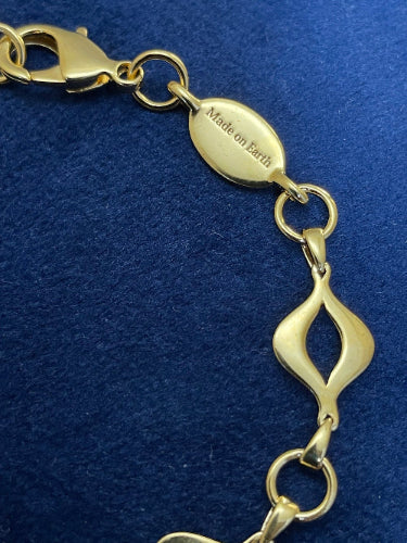 Detail of engraved “Made on Earth” tag beside lobster clasp on the gold-plated Sacred Mandorla Bracelet by Angel Aberdeen.