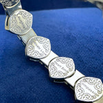 Close-up of engraved 14-karat white gold bracelet links with words like Laughter, Cultivate Love, Heart Smile, and Compassion on a royal blue background.
