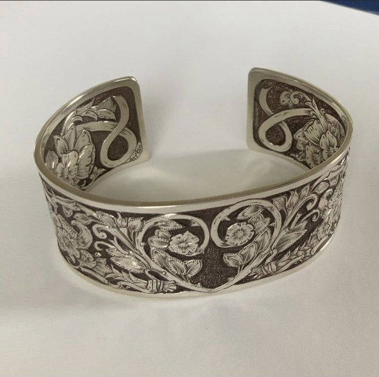 Front image Hand-engraved sterling silver cuff.  Floral Montana rose engraving covers the entire front.  A one-of-a-kind bracelet celebrating strength, healing, and rebirth.